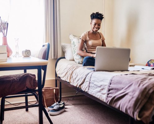 College dorm living with student studying on dorm room bed