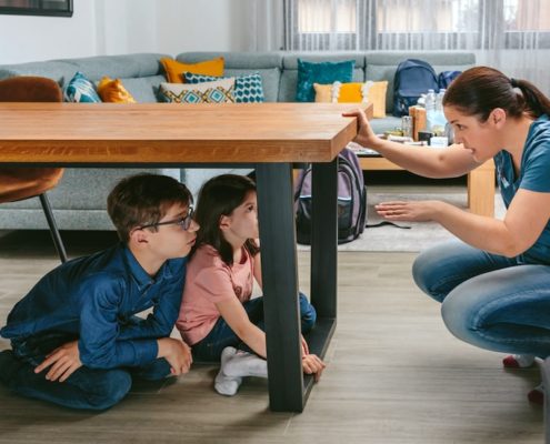 Emergency and Earthquake Preparedness Safety Drill as Mother guides her children under the table